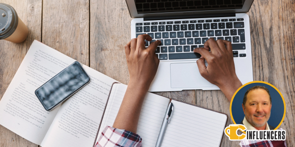 Image of a workspace with an open book, phone and person typing on a computer